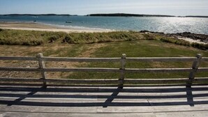 Een houten bankje met uitzicht op een strand, een grasveld en een rotsachtige kustlijn.
