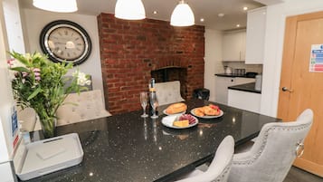 A modern kitchen with a brick wall, a clock, and a dining area with two chairs and a table set with food and drinks.