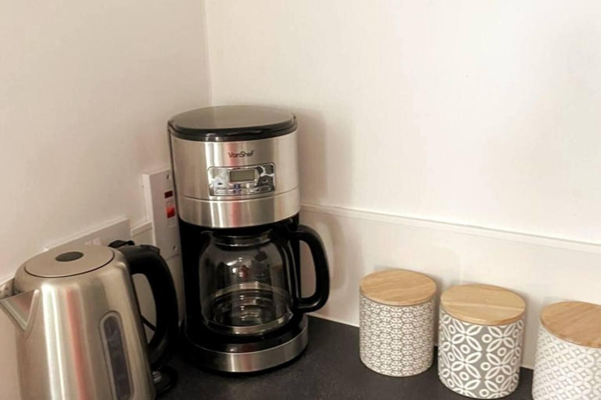Une machine à café est posée sur un plan de travail, avec deux récipients décorés placés à côté.