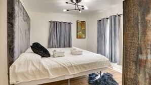 Une chambre moderne avec un grand lit, des rideaux gris, un luminaire au plafond et un plancher en bois.
