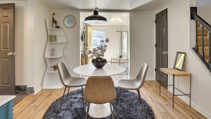 Un coin repas comprenant une table ronde, quatre chaises, un tapis noir et un luminaire suspendu.
