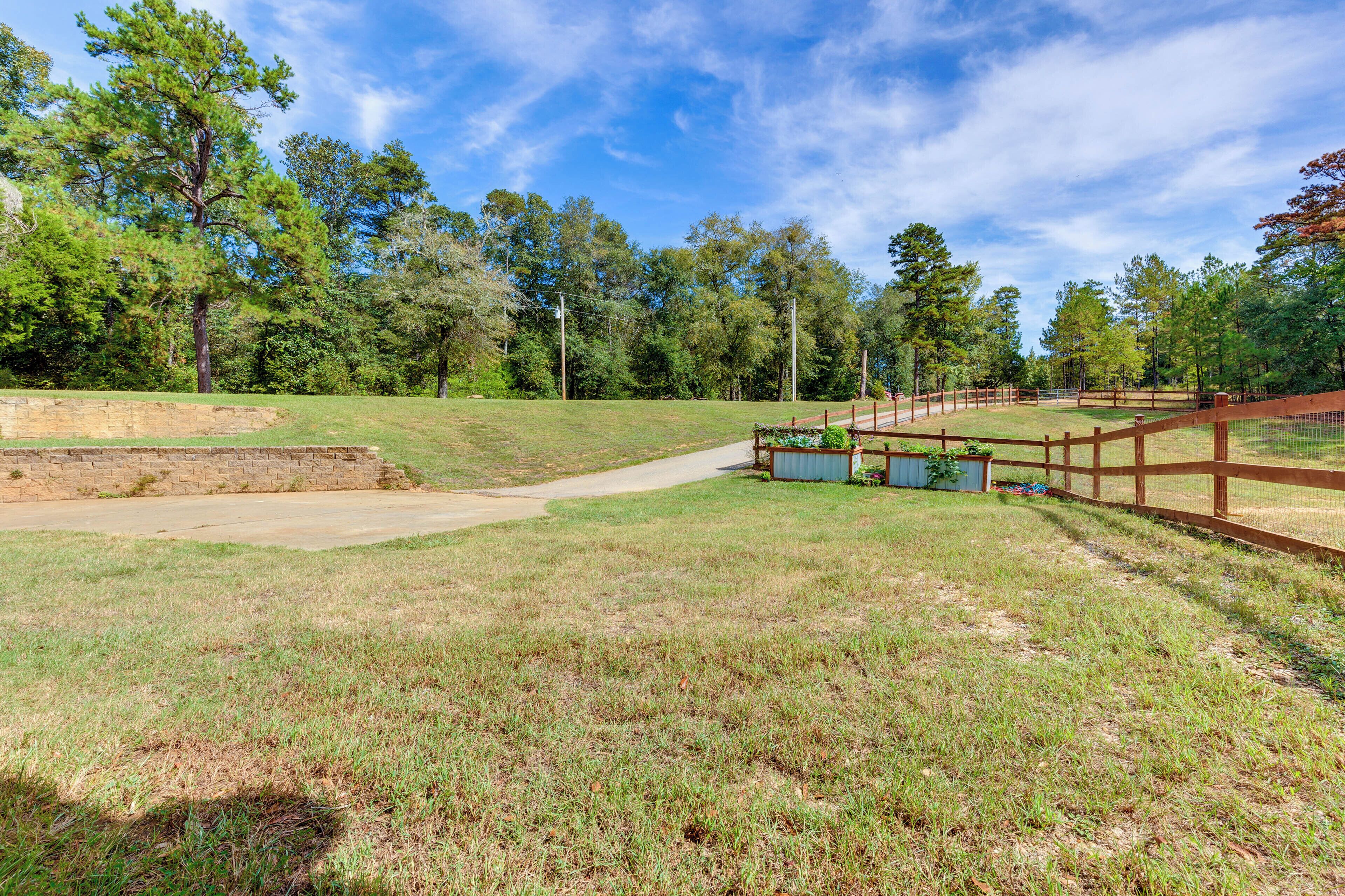 A grassy area with a wooden fence, a concrete path, and trees in the background.