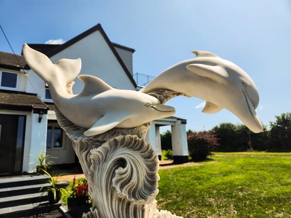 Una escultura de dos delfines sobre un pilar decorativo frente a una casa.