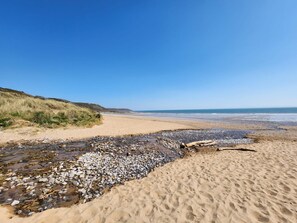 Una playa de piedras y arena, una colina cubierta de hierba y el océano al fondo.