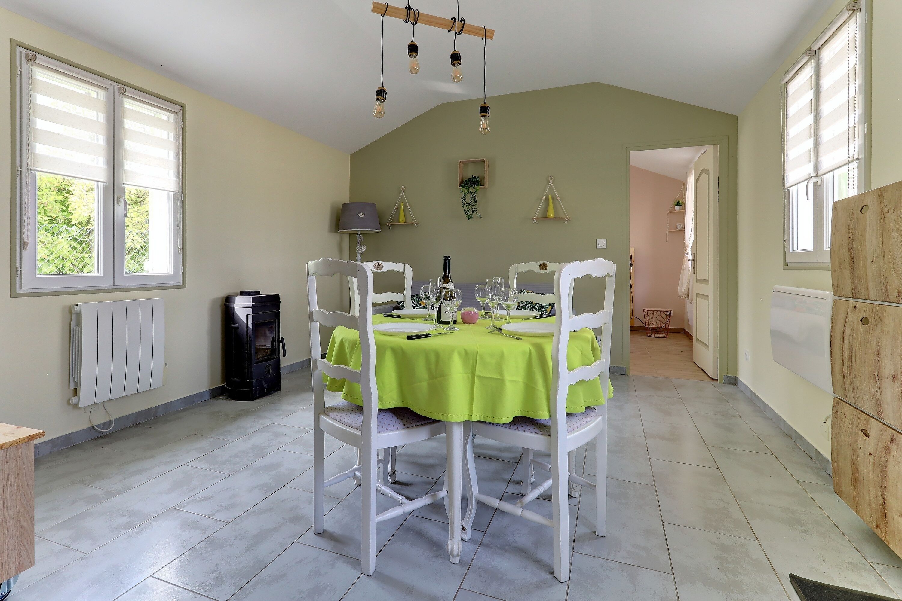 Zona pranzo con tavolo imbandito per quattro persone, sedie bianche, tovaglia verde e lampadario.