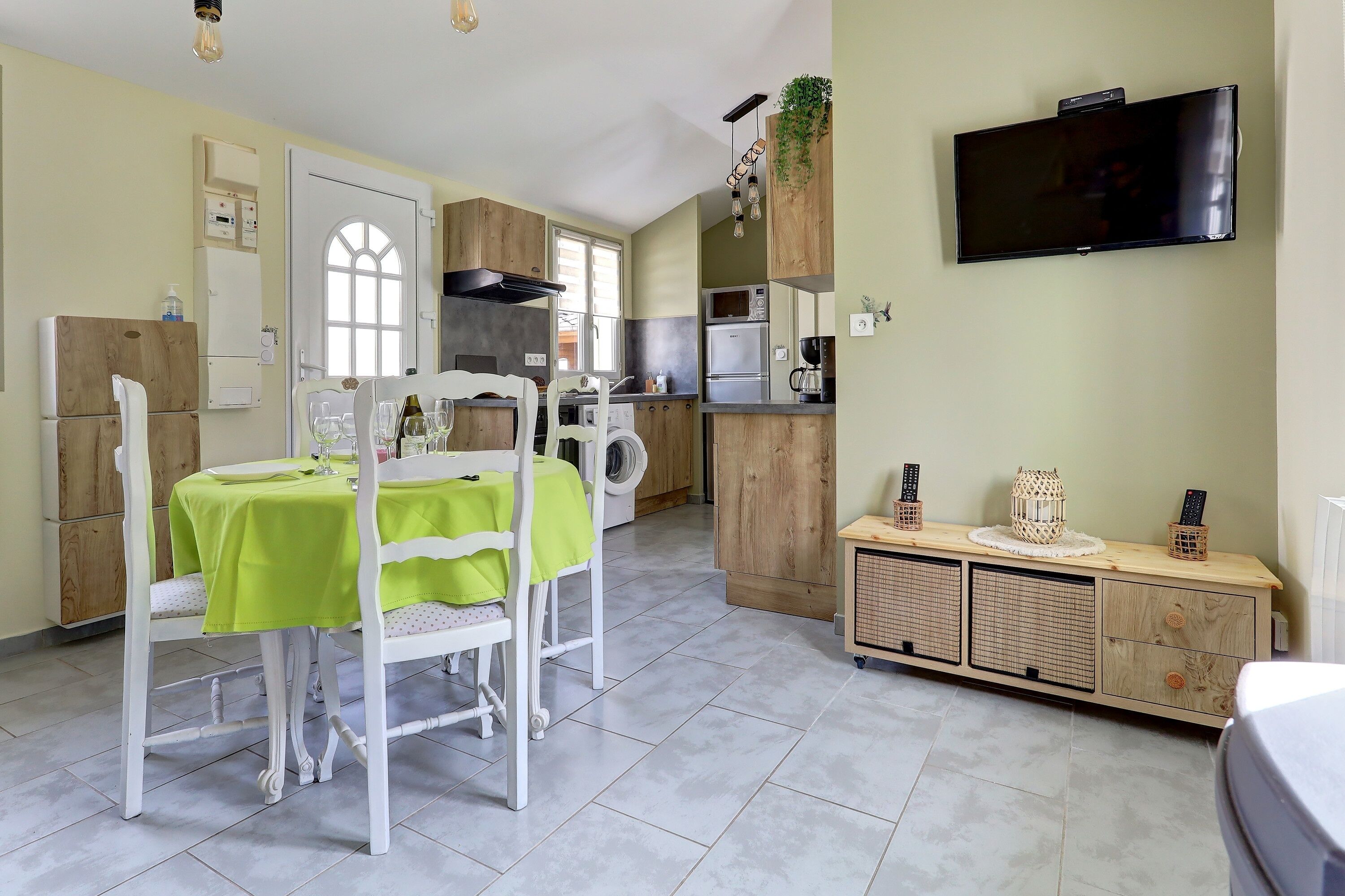A compact kitchen with a dining area, a TV mounted on the wall, and a built-in washing machine.