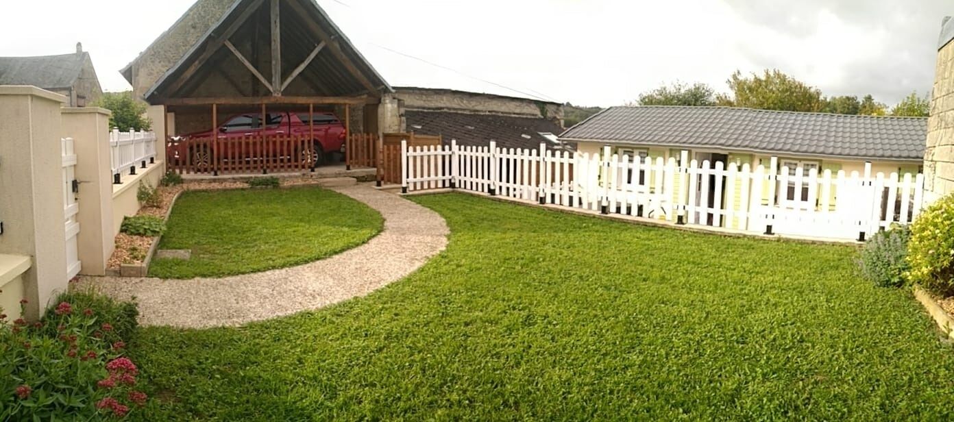 A well-maintained lawn with a white picket fence, a covered car parking area, and a building with a pitched roof.
