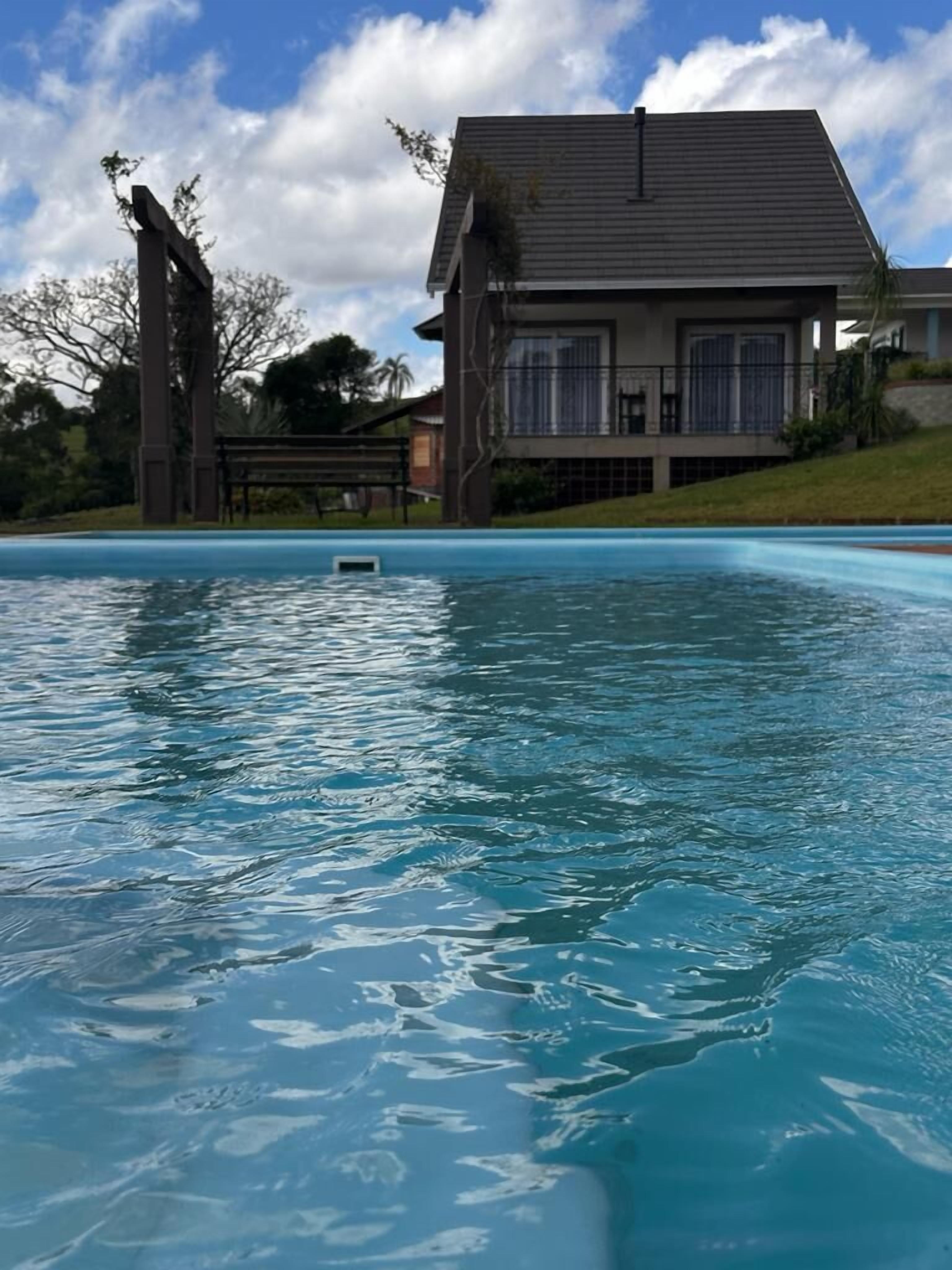 Een zwembad met helderblauw water, omgeven door gazon en een huis met schuine kap.