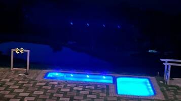 Área de piscina com um caminho de tijolos que a leva, cercada por grama e uma pequena planta.