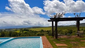 Une piscine rectangulaire bordée de briques, entourée d’une pelouse agrémentée d’une pergola et de quelques sièges.