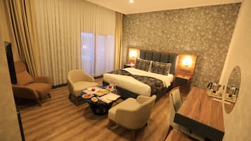 Een hotelkamer met een groot bed, twee nachtkastjes, een bureau, een stoel, een kleine tafel met eten en een bank.