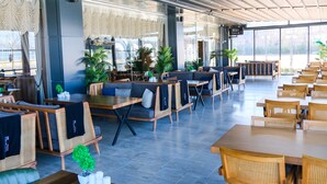 Un espacio interior amplio con arreglos de asientos que incluyen sofás y mesas, ventanas grandes y plantas en macetas.