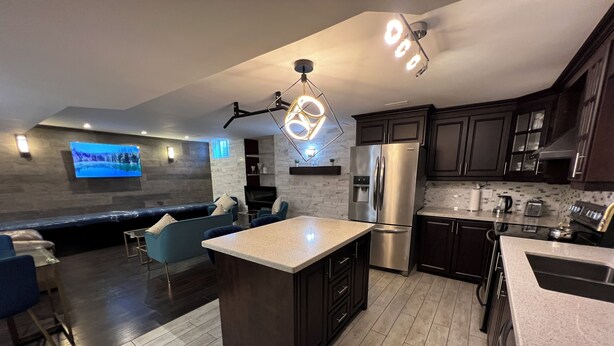 A modern kitchen with dark cabinetry, a central island, stainless steel appliances, and a built-in TV.