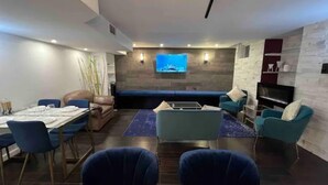 A modern living room with a dining area, a large flat-screen TV mounted on the wall, and a fireplace.