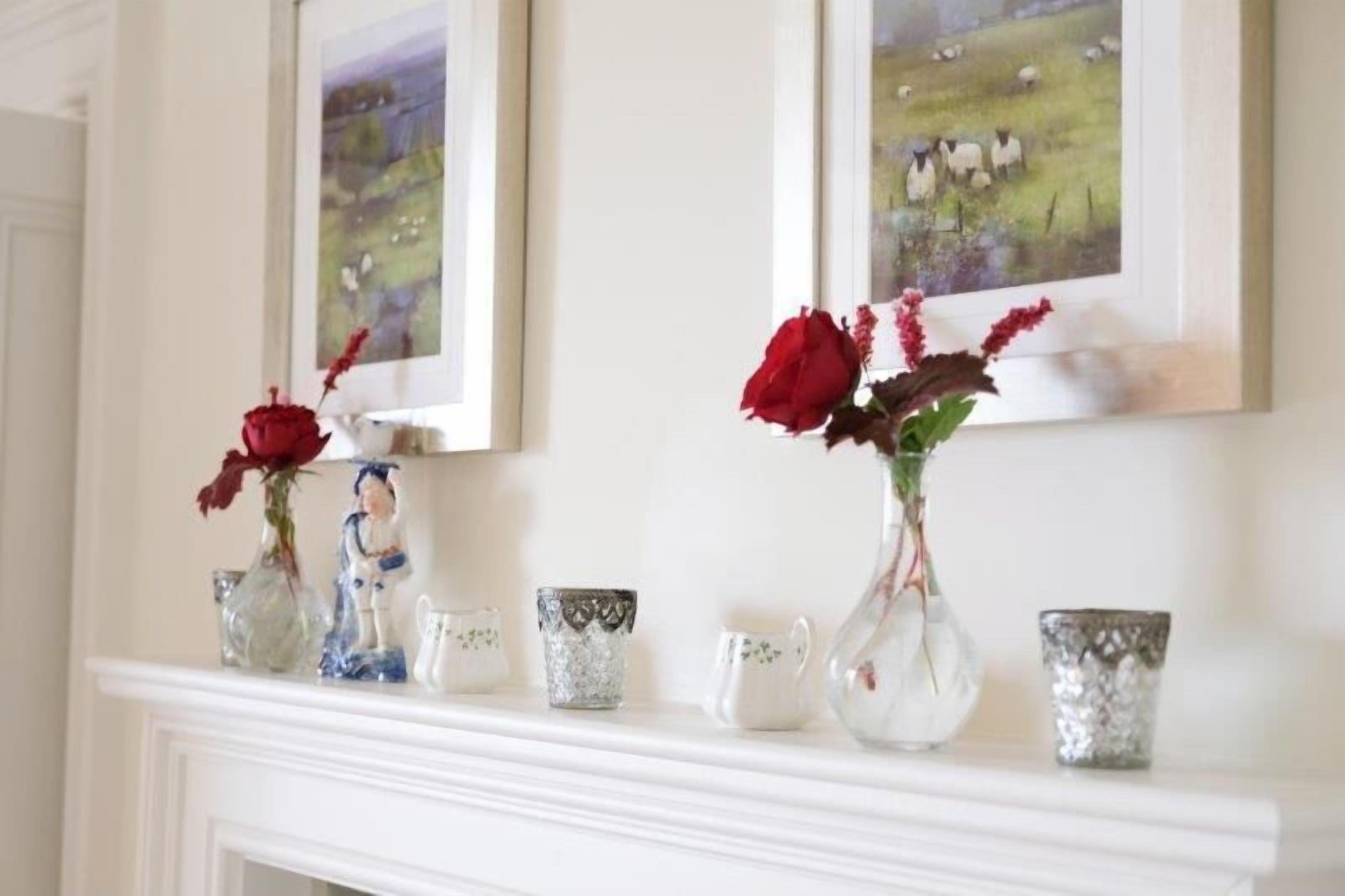 A fireplace mantel with decorative items including vases with red roses and figurines, and framed artwork above.