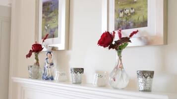A fireplace mantel with decorative items including vases with red roses and figurines, and framed artwork above.
