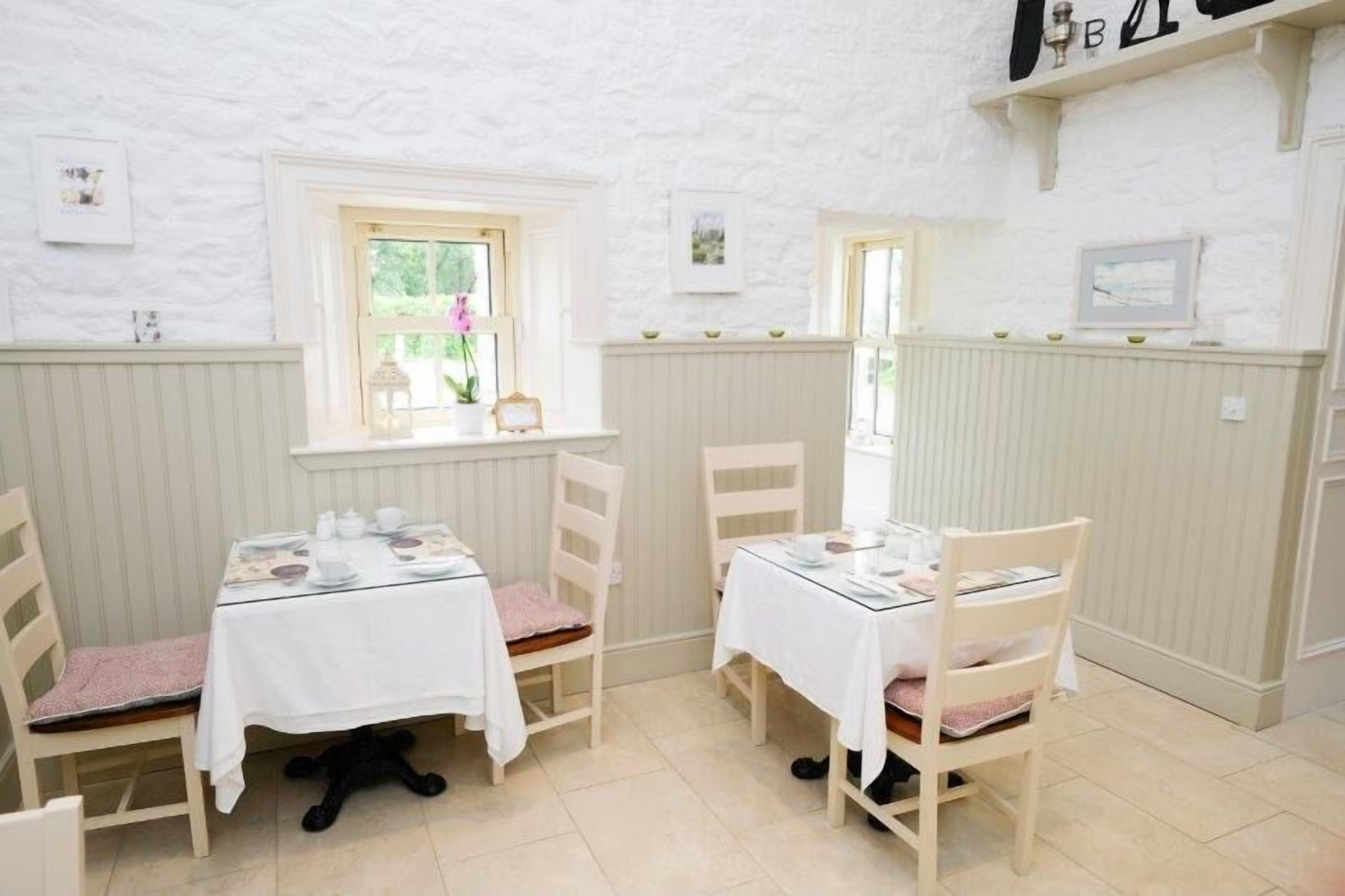 A cozy dining area with two tables set for two, white walls, and a window with a view.