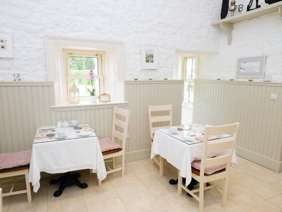 A cozy dining area with two tables set for two, white walls, and a window with a view.