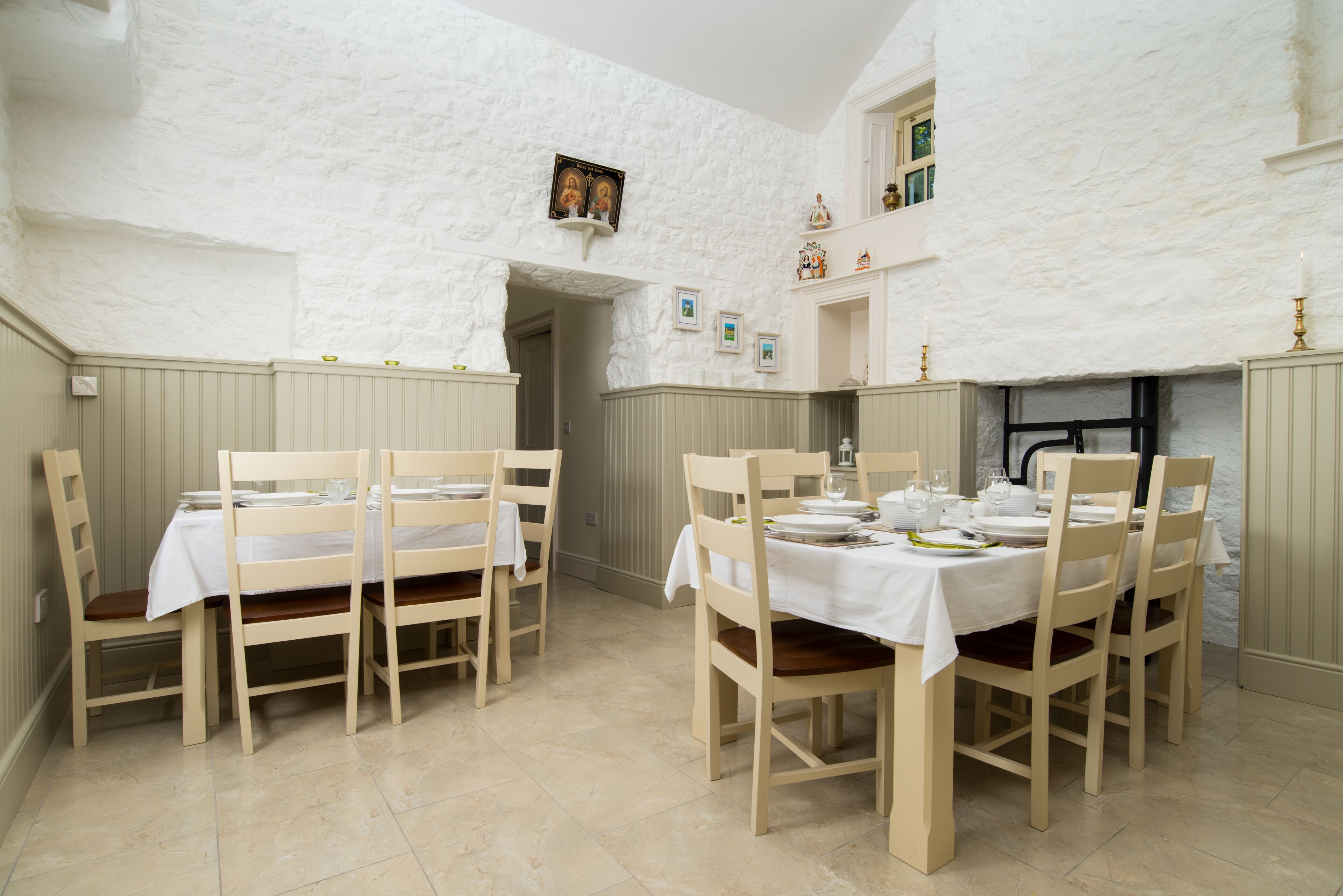 Un espace repas avec un mur blanc à texture, des chaises et des tables en bois, et une petite porte donnant sur une autre pièce.