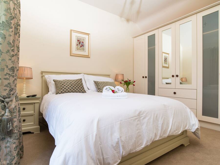 A neatly made bed with a white comforter and pillows, a bedside table with a lamp, and a wardrobe with glass doors.
