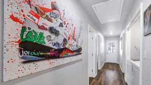 A hallway with a large graffiti-style artwork on the wall, wooden flooring, and white walls. - Rashali kicks theme house in SA (San Antonio)