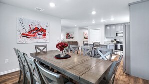 A modern dining area with a wooden table, grey chairs, and a large red sneaker artwork on the wall. - Rashali kicks theme house in SA (San Antonio)