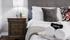 A neatly made bed with white bedding, a grey headboard, and a bedside table with a lamp, a small plant, and a tray of rolled towels. - Rashali kicks theme house in SA (San Antonio)
