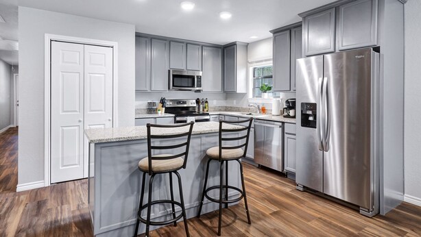 A modern kitchen with grey cabinets, stainless steel appliances, and a wooden floor. - Rashali kicks theme house in SA (San Antonio)