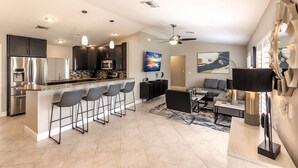 A modern kitchen with a central island, bar stools, and a dining area with a sofa and table. - Fun in the Sun! Pool, Fenced Yard, Ping Pong, BBQ (Naples)