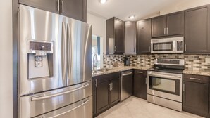 A modern kitchen with stainless steel appliances, dark cabinetry, and a tiled backsplash. - Fun in the Sun! Pool, Fenced Yard, Ping Pong, BBQ (Naples)