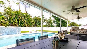 A poolside dining area with a table, chairs, and a grill. - Fun in the Sun! Pool, Fenced Yard, Ping Pong, BBQ (Naples)