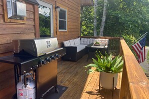 A wooden deck with a barbecue grill, outdoor seating, and an American flag. - Last Leaf Days | Mountain Hot Tub & Sauna (Maggie Valley)