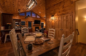 A wooden interior with a dining table, chairs, a television, and a fireplace.