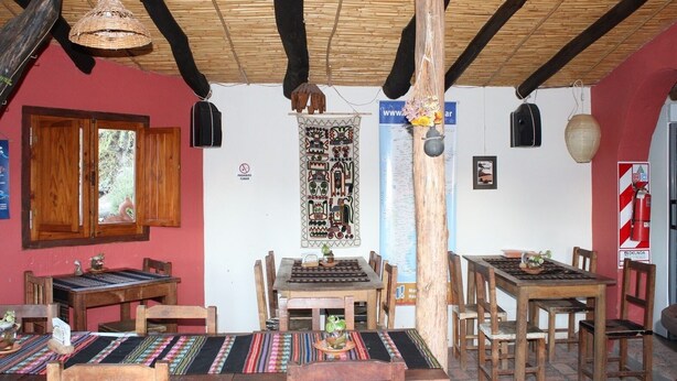 A rustic dining area with wooden tables and chairs, a woven ceiling, and a large tapestry on the wall. - El Sol Hostel y Posada Humahuaca (Humahuaca)