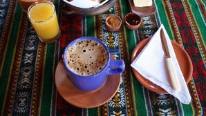 A breakfast setting with a cup of coffee, a glass of orange juice, a bowl of pastries, a plate with butter, and a napkin. - El Sol Hostel y Posada Humahuaca (Humahuaca)