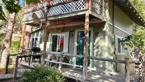 A rustic cabin with a wooden porch, a lattice railing, and a deer head decoration. - NorthFork Lodge Cabin #2 "The Pine" (West)