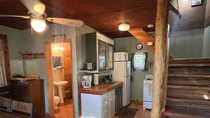 A compact kitchen with a sink, stove, and cabinets, a wooden dining table, and a ceiling fan. - NorthFork Lodge Cabin #2 "The Pine" (West)