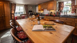 Una mesa de comedor de madera con sillas, una botella de vino, copas y un libro.