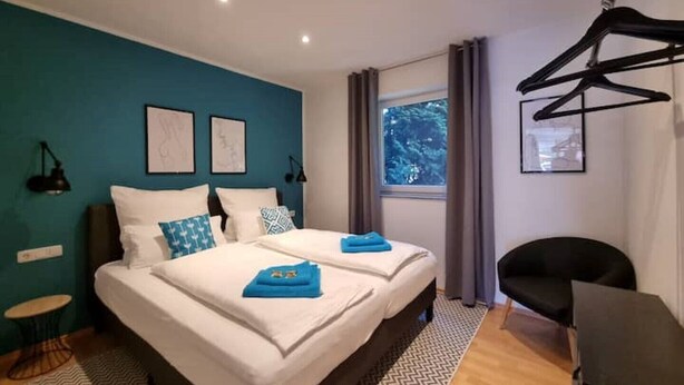 Moderni hotellihuone, jossa on suuri sänky, kaksi yöpöytää, työpöytä ja ikkuna, jossa on verhot.
