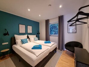 Een moderne hotelkamer met een groot bed, twee nachtkastjes, een bureau en een raam met gordijnen.