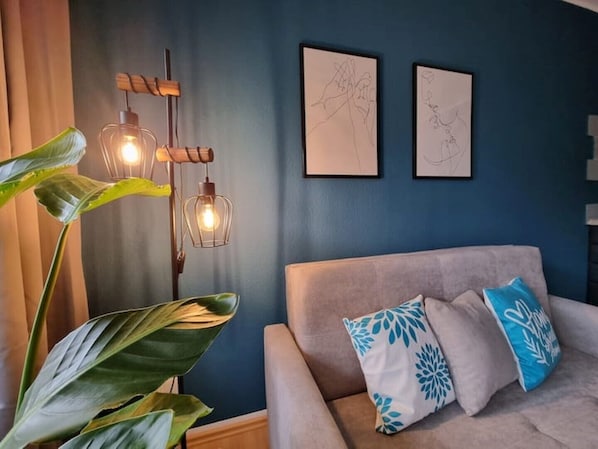 Ett rum med en grå soffa, två abstrakta konstverk som hänger på väggen, en modern golvlampa och en stor grön växt.