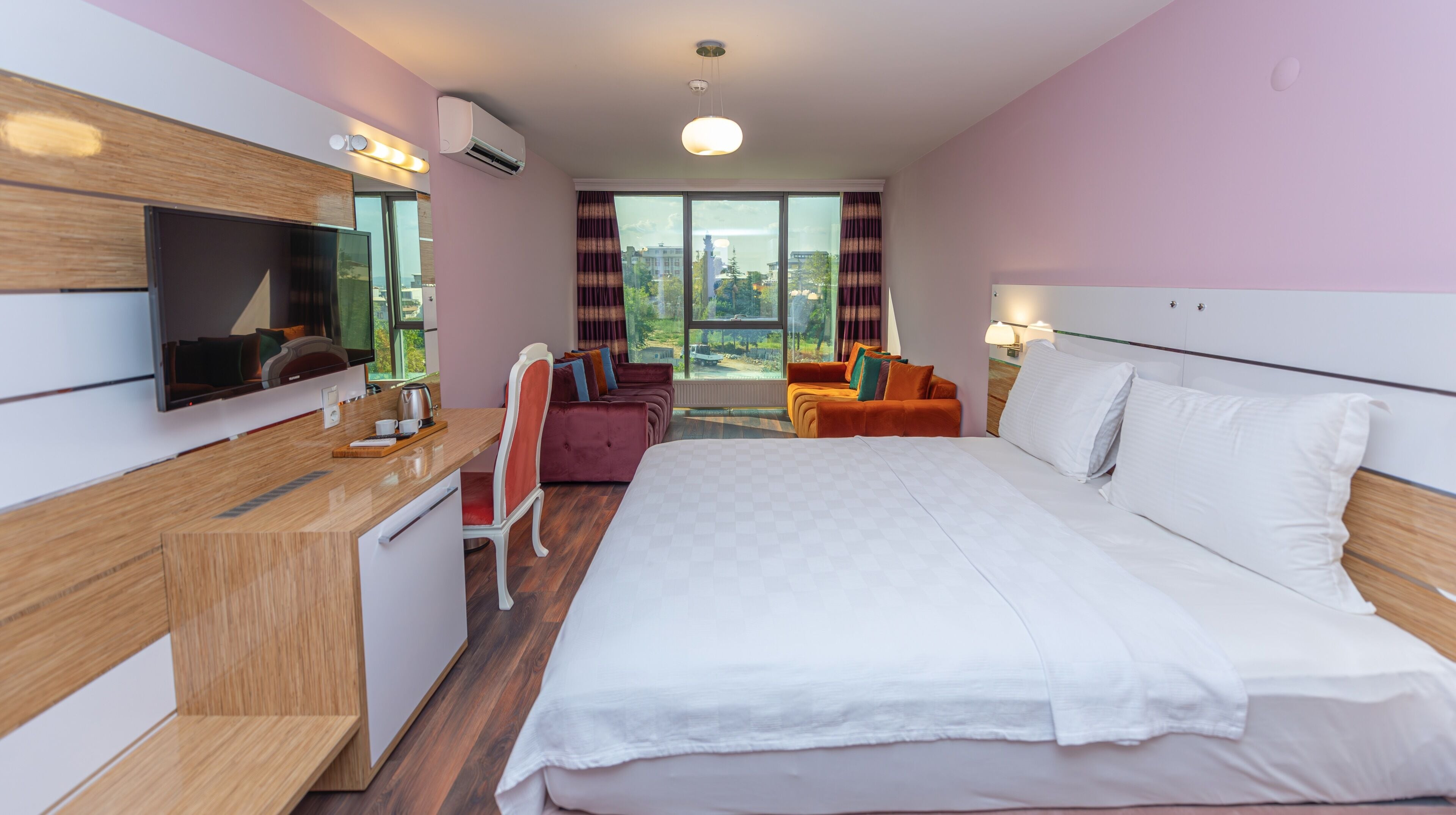 A modern hotel room with a large bed, a desk with a flat-screen TV, and a seating area with two sofas.