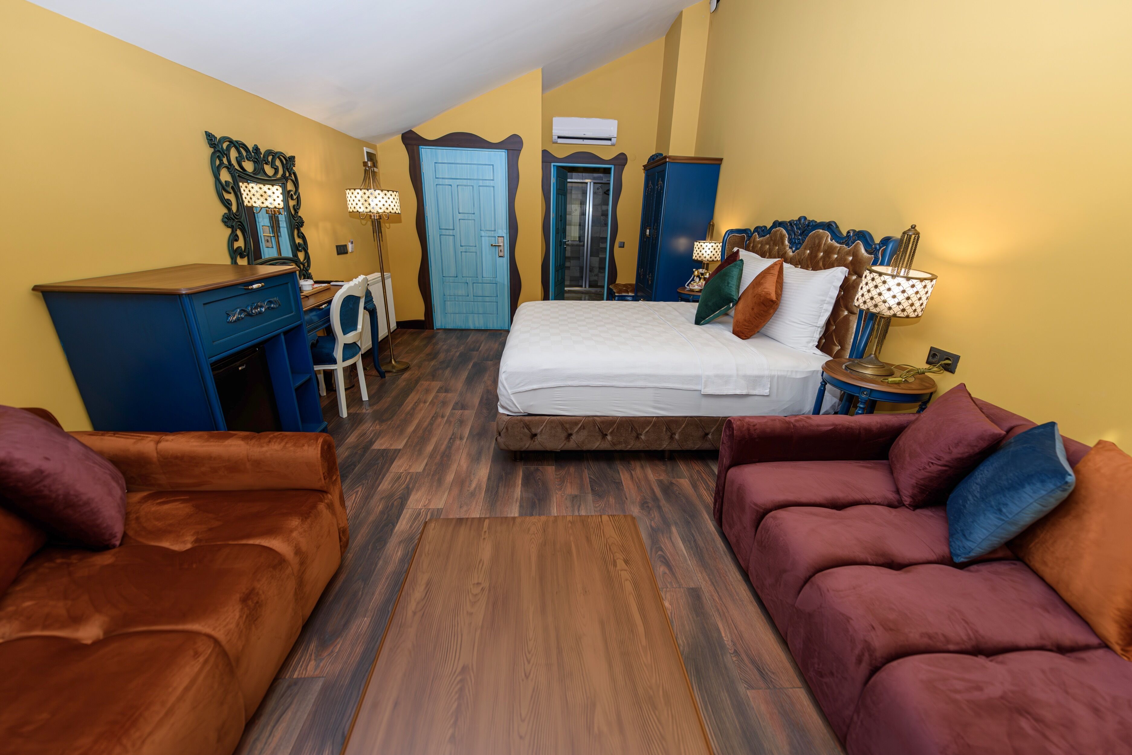 A bedroom with a bed, a desk, a chair, and two sofas.