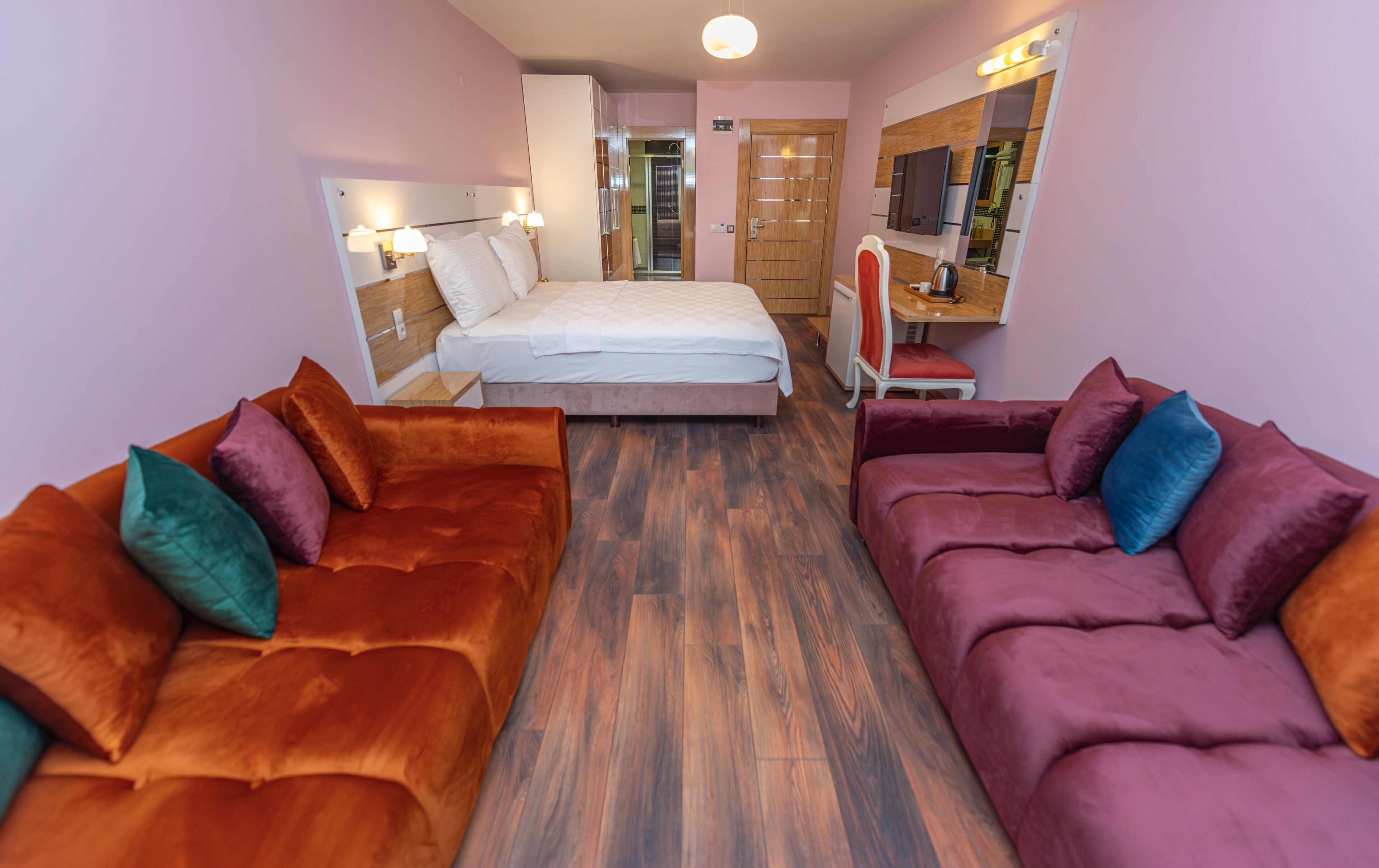A modern hotel room with a bed, two sofas, a small table, and a mirror.