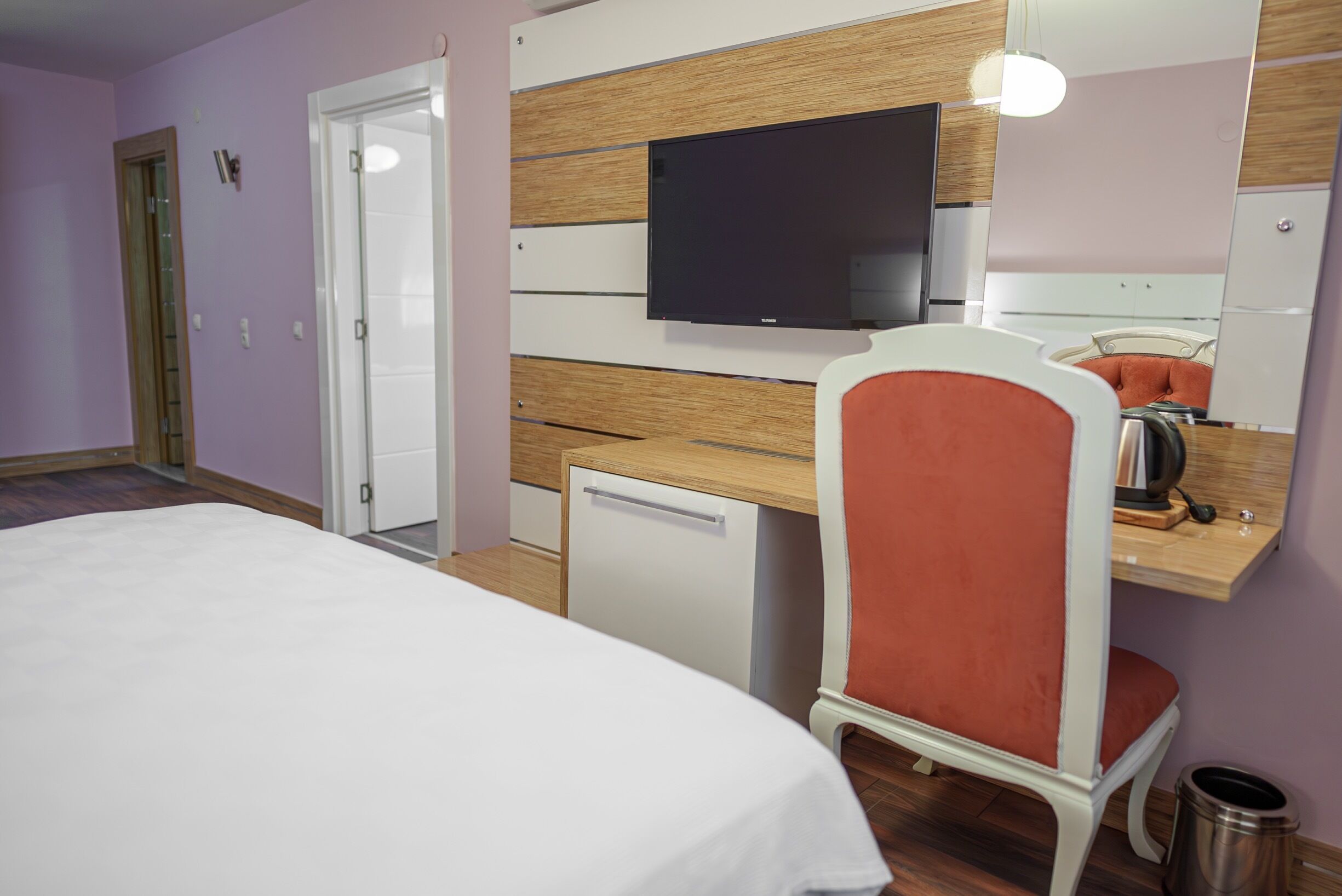 Una habitación de hotel con una cama, un escritorio con silla, un televisor y un espejo.