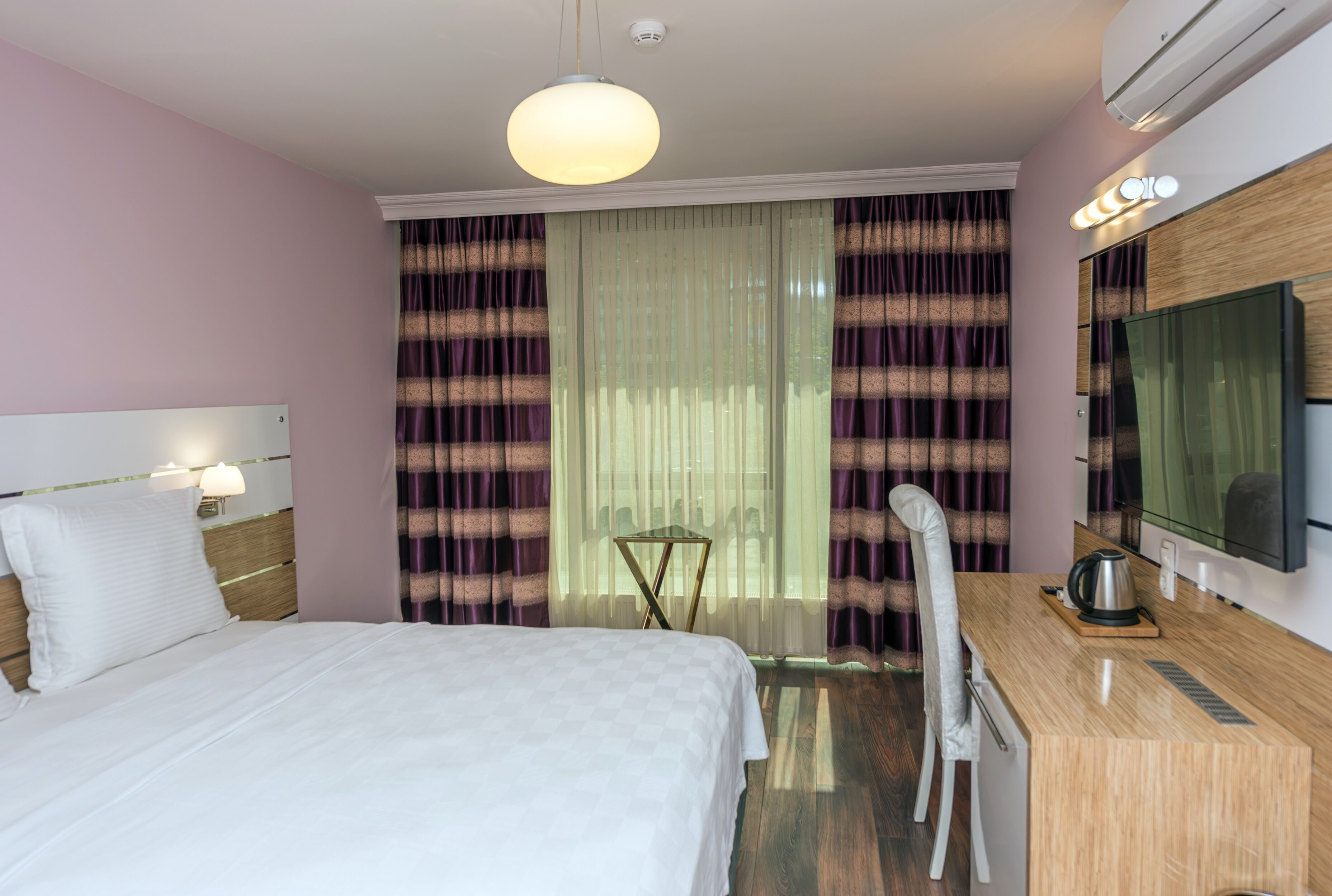 A hotel room with a bed, a desk with a chair, a television, and curtains.