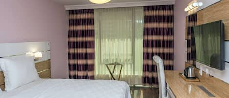 Una habitación de hotel con una cama, un escritorio con una silla, un televisor y cortinas.