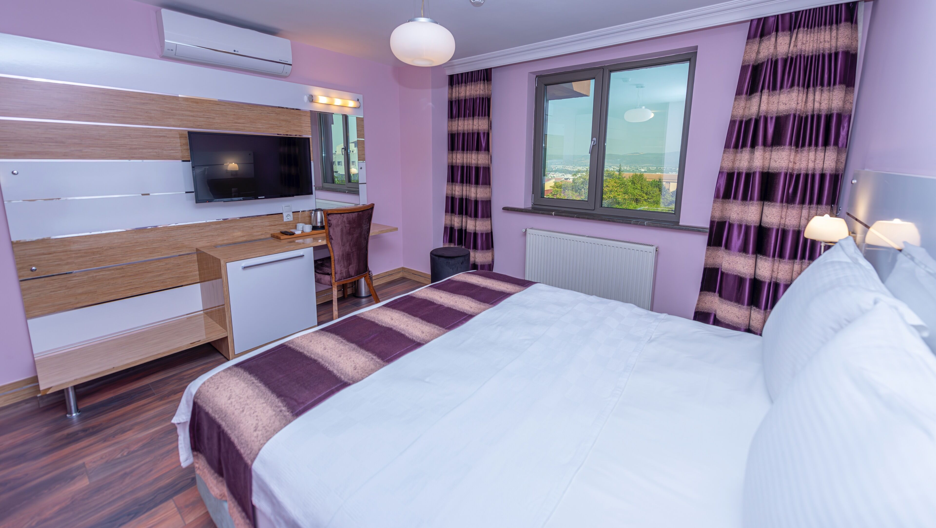 A modern hotel room with a bed, a desk, a chair, a television, and a window with curtains.