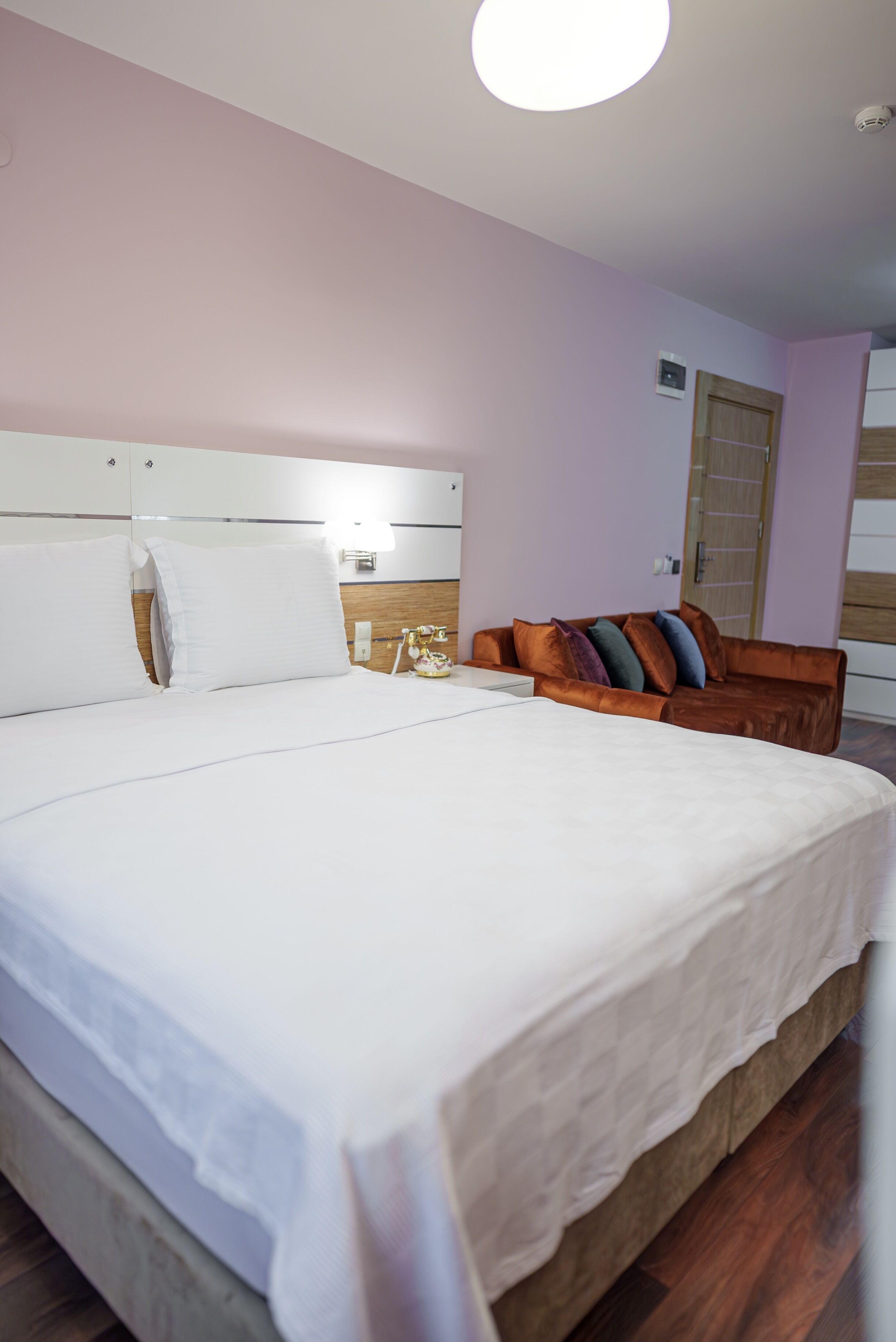 A neatly made bed with white linens, a wooden headboard, and a brown leather sofa with cushions.