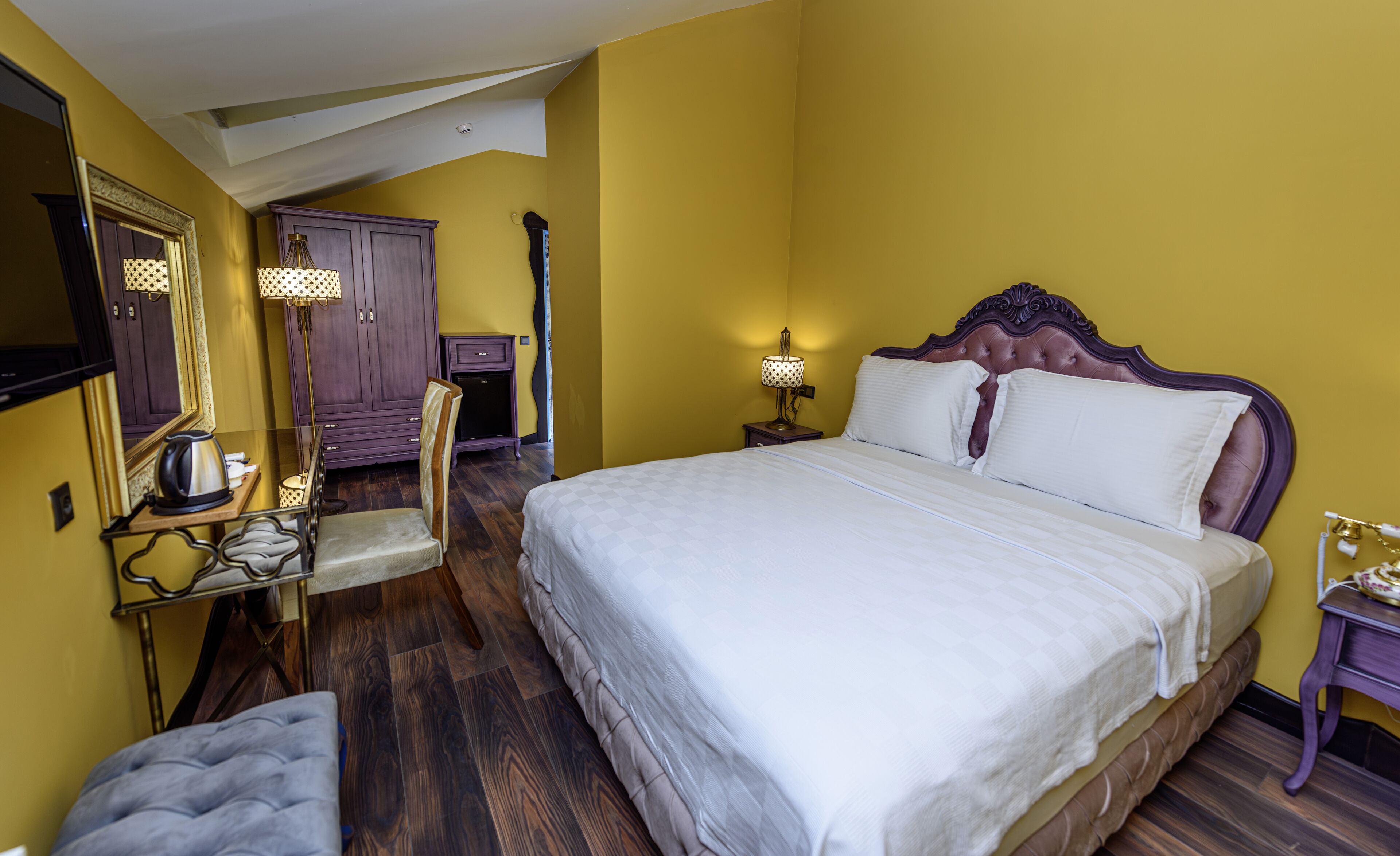 Ein Hotelzimmer mit einem großen Bett, Holzboden, Spiegel, Nachttisch mit Lampe und Kleiderschrank.